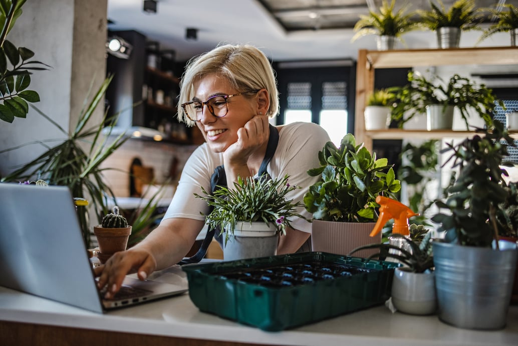 Young botanist checking online orders on laptop after using the right eCommerce tools to grow her business - Shift4Shop