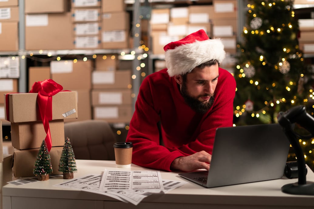 Man wearing a Santa hat managing his holiday sales taxes on a laptop - Shift4Shop